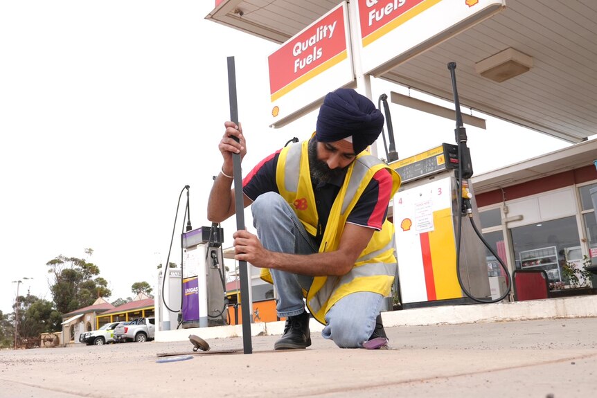 An Indian man holding a long rod pulled from underground fuel tank at a service station