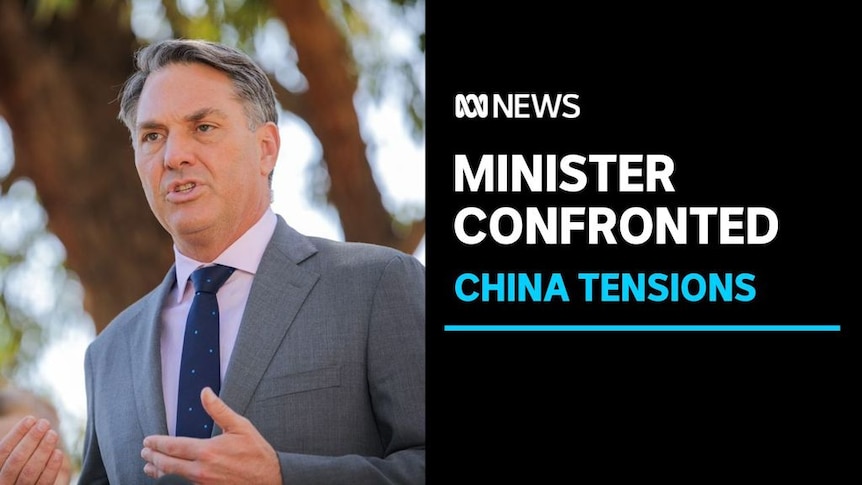 Minister Confronted, China Tensions: Richard Marles wears grey suit outside with gumtree silhouettes behind him. 