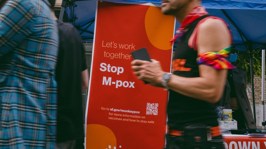 Man walks past a stand dispersing information on mpox at a street festival