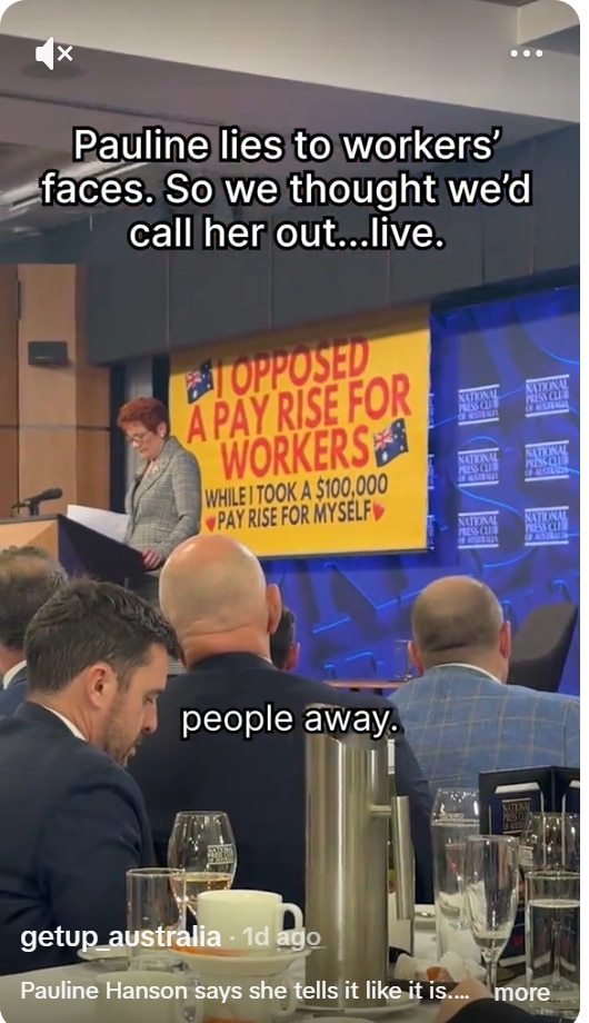 A woman speaking at a lectern with a yellow banner behind her.