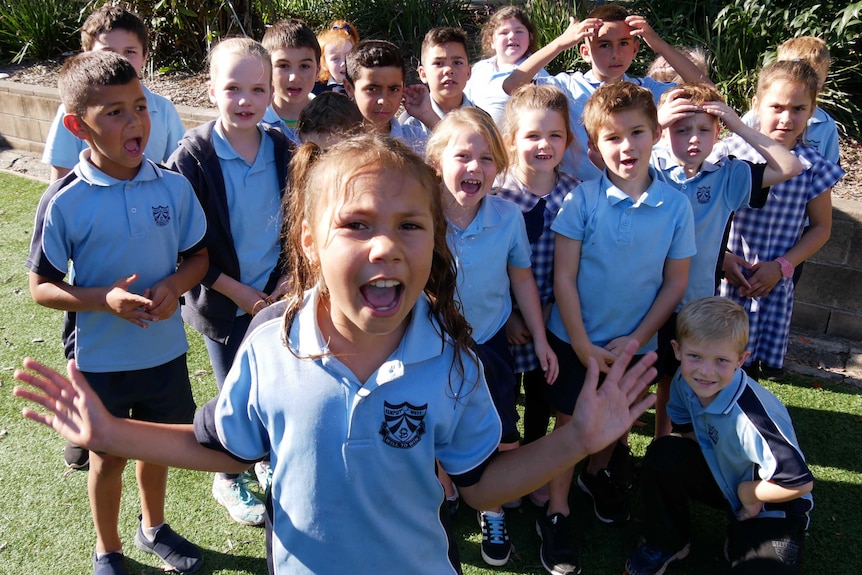 Eight year old girl in her school uniform standing in front of her classmates outside in the playground