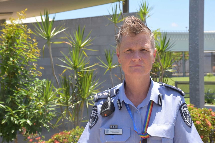 Woman with short blond hair in corrections officer blue uniform looking with a straight face to the camera wears rainbow lanyard