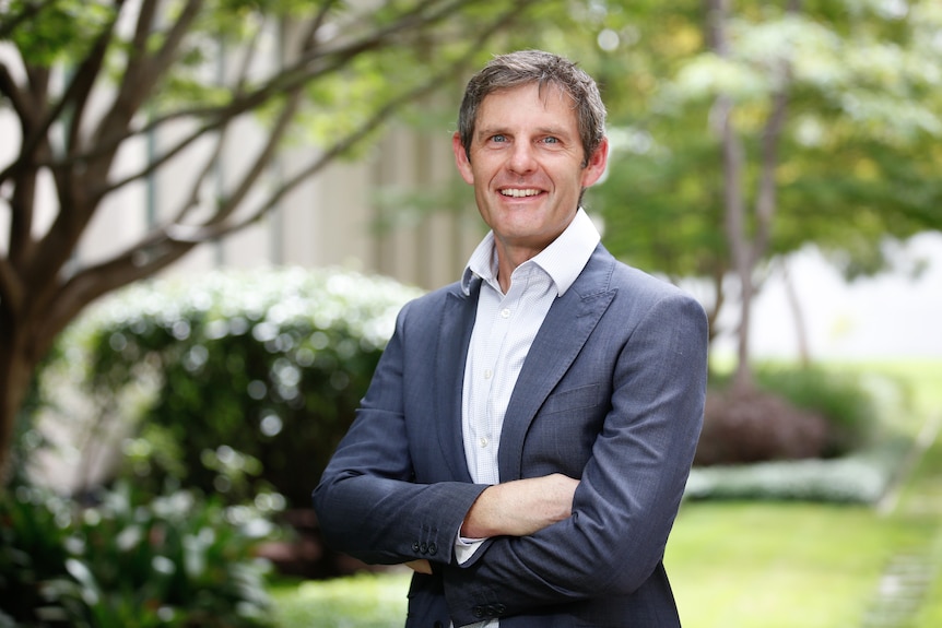 A man in a suit with his arms crossed smiling.