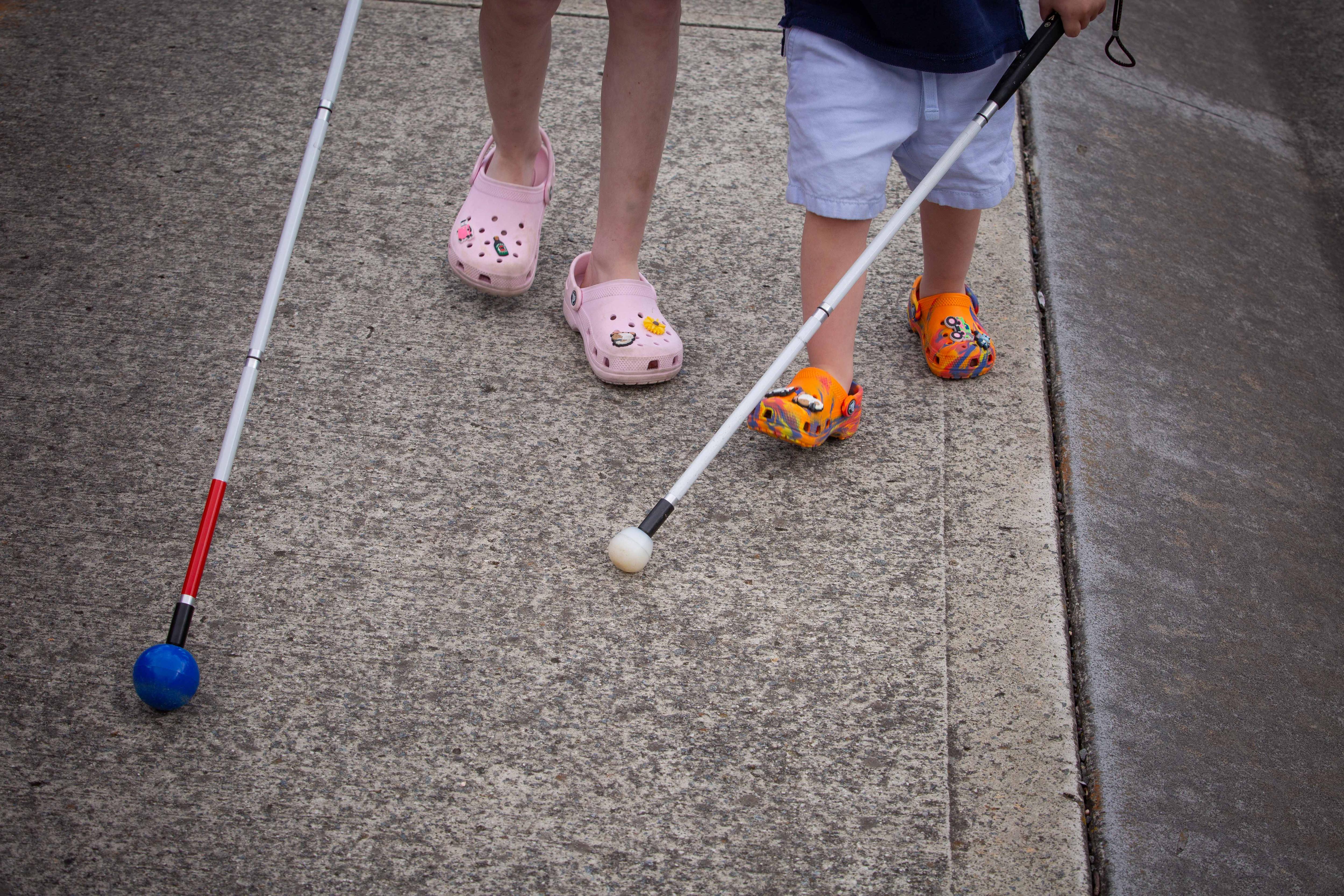 Muestra a dos niños caminando por la calle con palos desde las rodillas para abajo. 