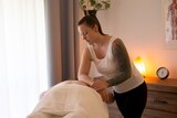 A woman leans on a person's back in a massage therapy studio with a lamp in the background.
