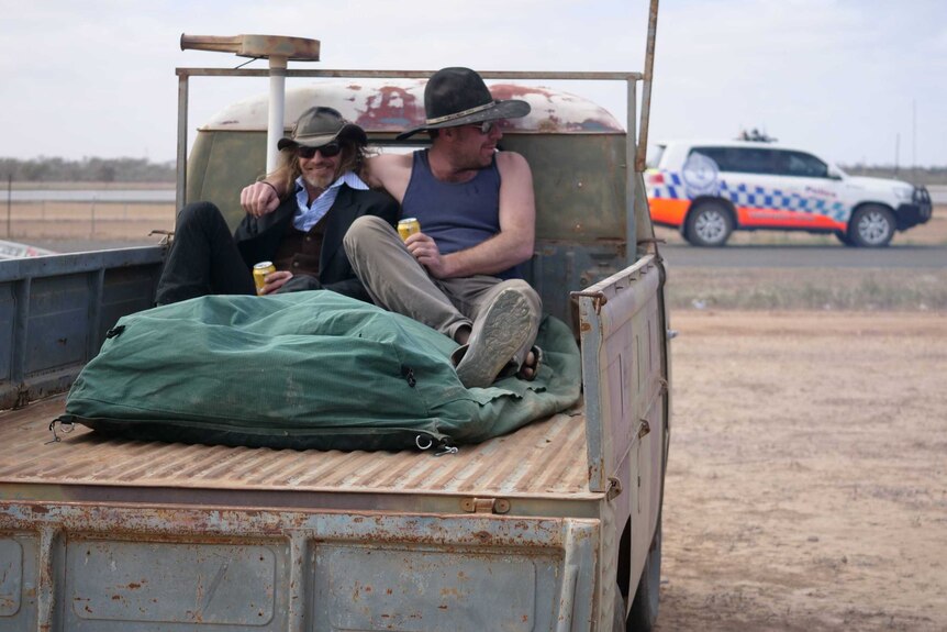 Two men sit drinking beer on the back of a ute.
