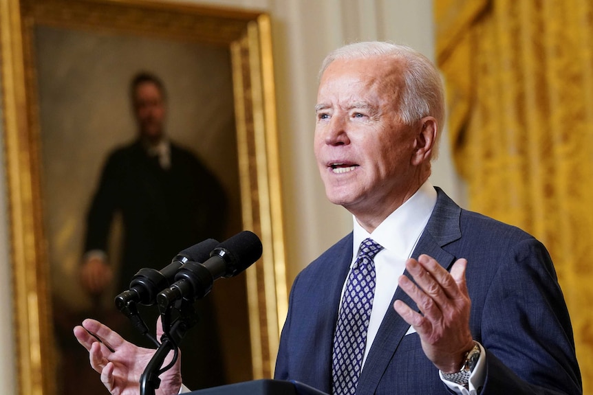 Biden gestures while giving a speech in front of an old portrait