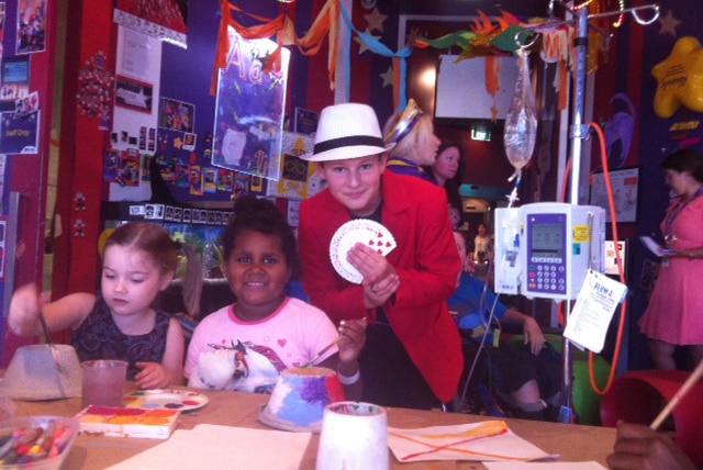 Small children paint as Magic Boy displays his cards in a room decked out in a Perth hospital