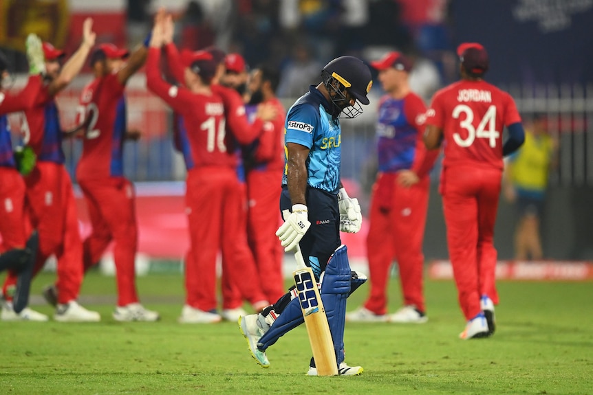 Kusal Perera walks with his head bowed as England players high five in the background