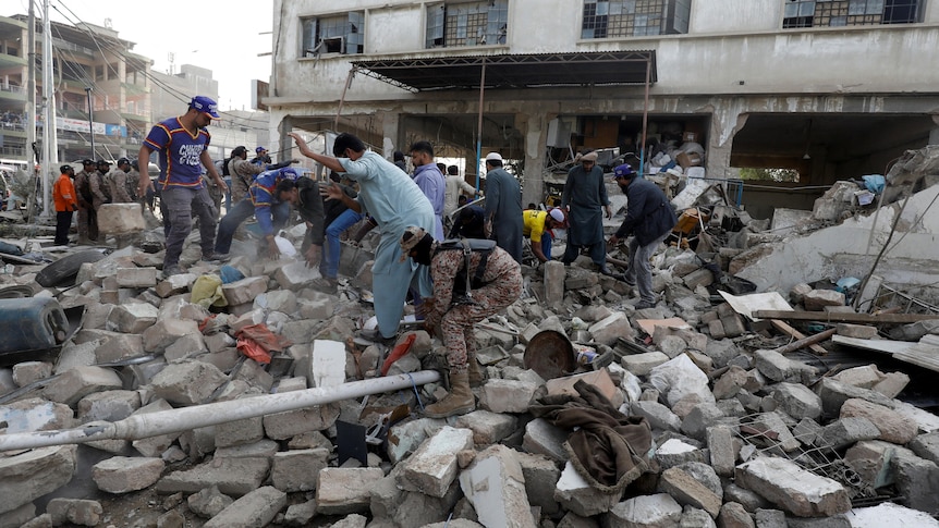 People and paramilitary personnel clear the rubble after a blast in an industrial area in Karachi.