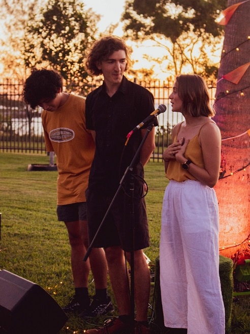 A young woman speaks into a microphone, standing with two other people