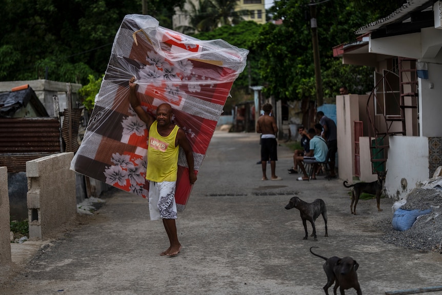 A man carries a mattress down a street. 