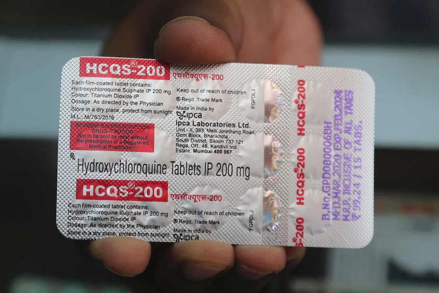 A close-up of a silver package of pills, with red writing, held by a hand.