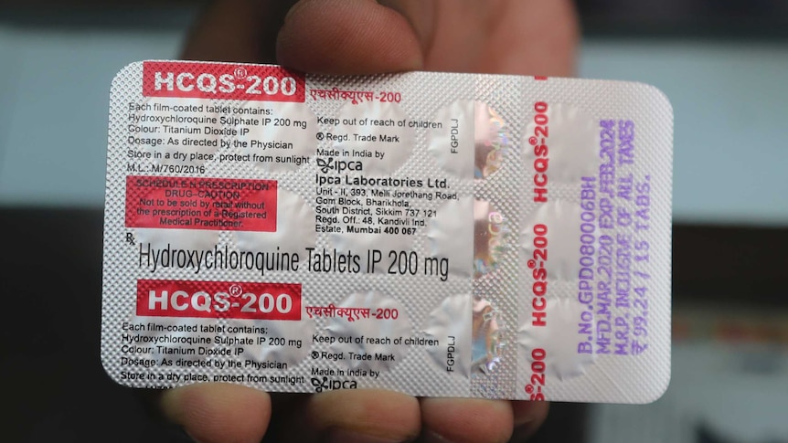 A close-up of a silver package of pills, with red writing, held by a hand.