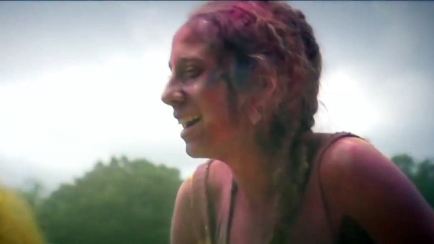 A smiling woman covered in coloured powder