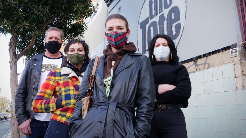 Three women and a man stand in front of a wall that says 'the Tote'