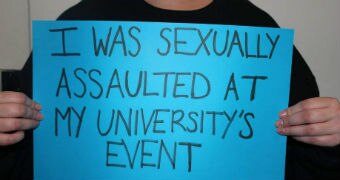 A person holds a blue poster with the words 'I was sexually assaulted at my university's event".