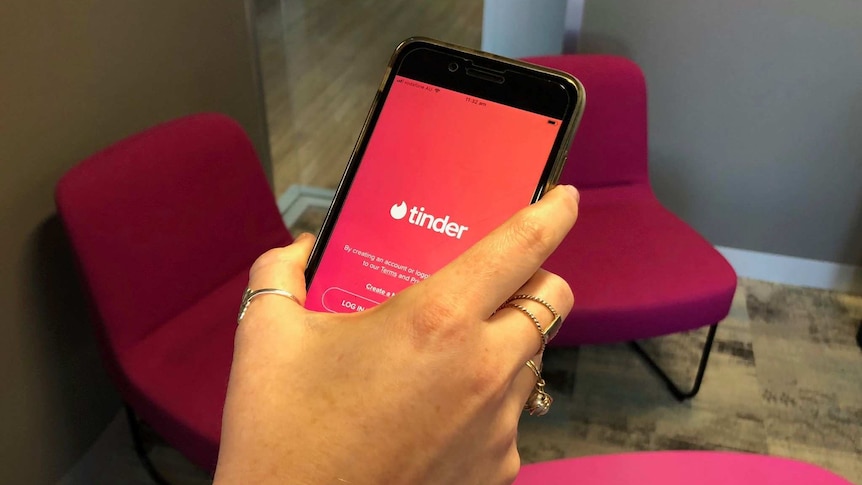 A hand holding a mobile phone with the Tinder application open on the screen