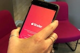 A hand holding a mobile phone with the Tinder application open on the screen