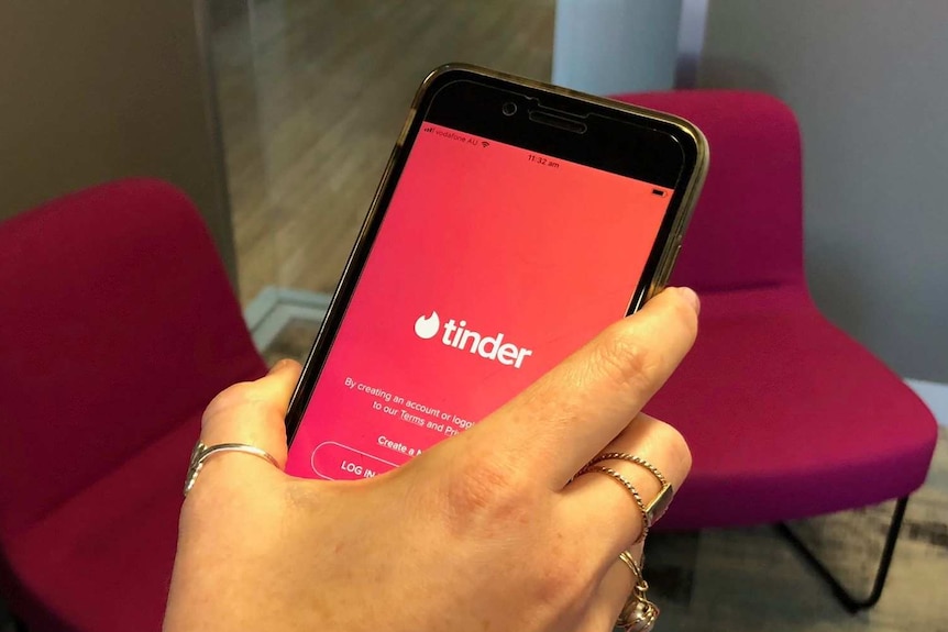 A hand holding a mobile phone with the Tinder application open on the screen