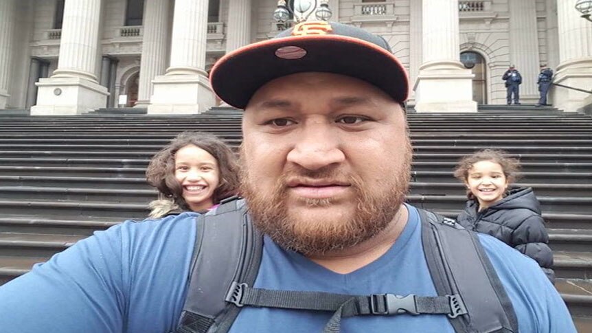 Clarence Leo posing for a selfie with two kids in the background on the steps of the Victorian Parliament.