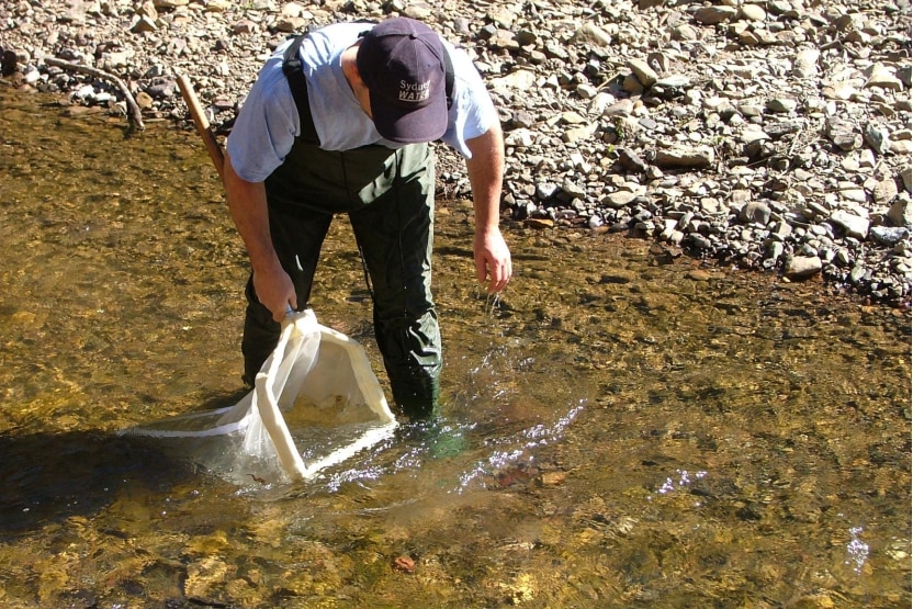 Man with bag scooping up water from creek 