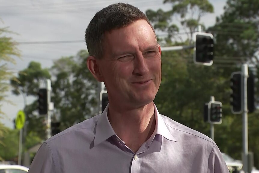 transport minister mark bailey standing on the side of the road in front of an intersection with traffic lights