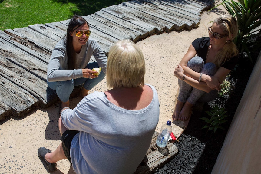 Three women sit together outside.