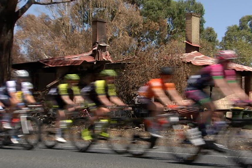Cyclists ride past a burnt house