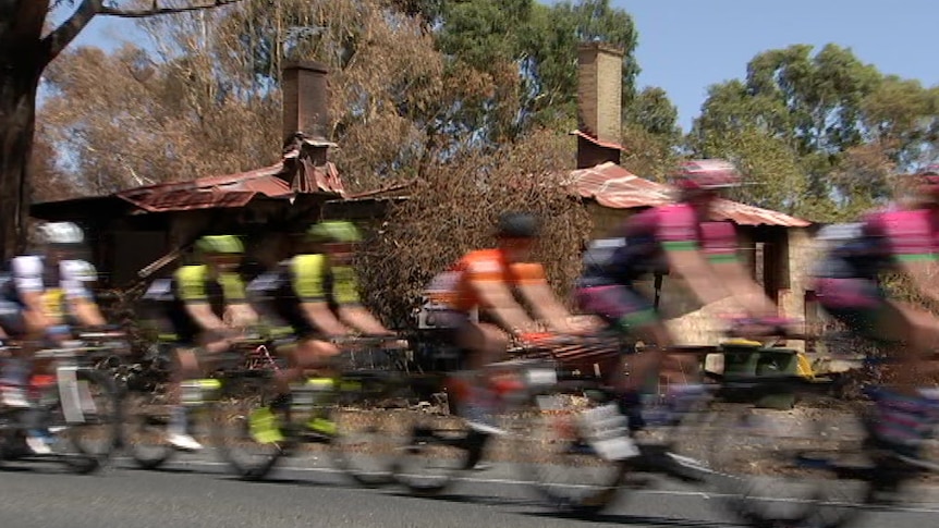 Cyclists ride past a burnt house