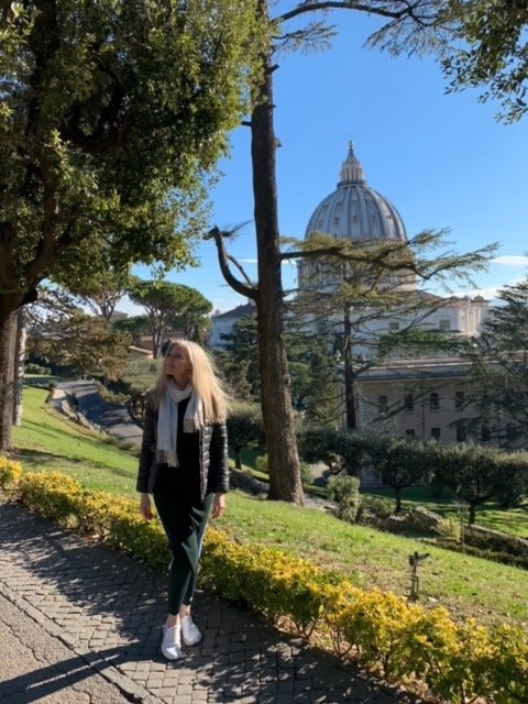 Joanne Bergamin posing for a photo inside the Vatican grounds with an historic dome in the background