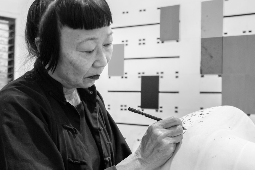 Lindy sits and works on a sculpture in a black and white image.
