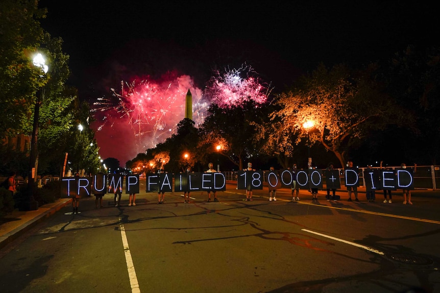 Protesters hold a lighted sign on a street as fireworks light up the sky around the Washington Monument