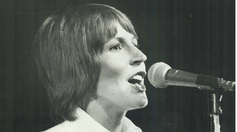 Helen Reddy sings into a microphone in a black and white image