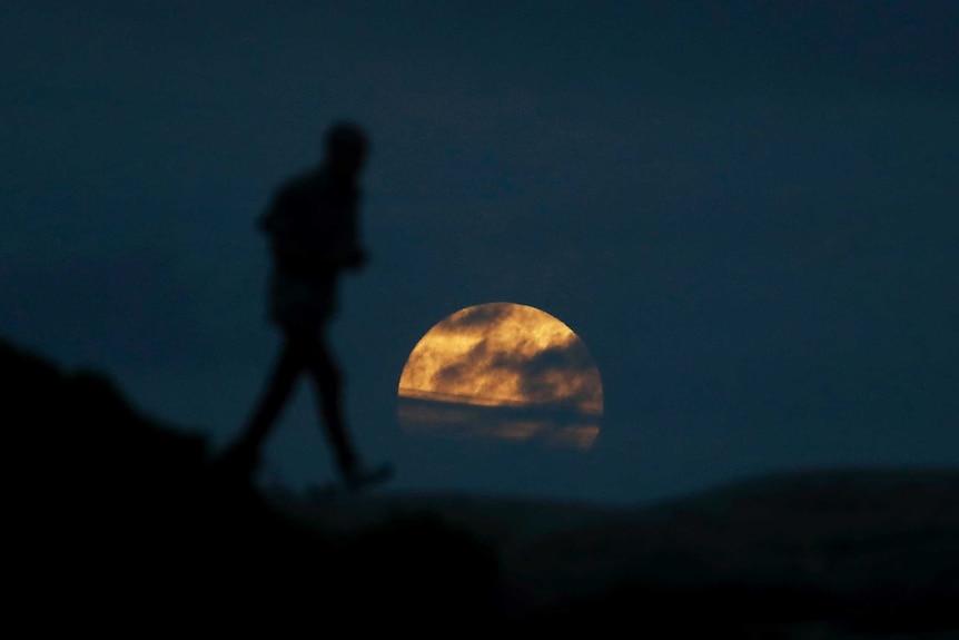 Silhouette of man in front of massive moon