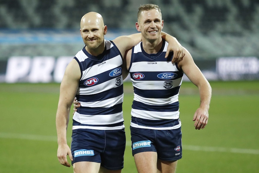 Two AFL stars leave the ground smiling with their arms around each other after milestone games.