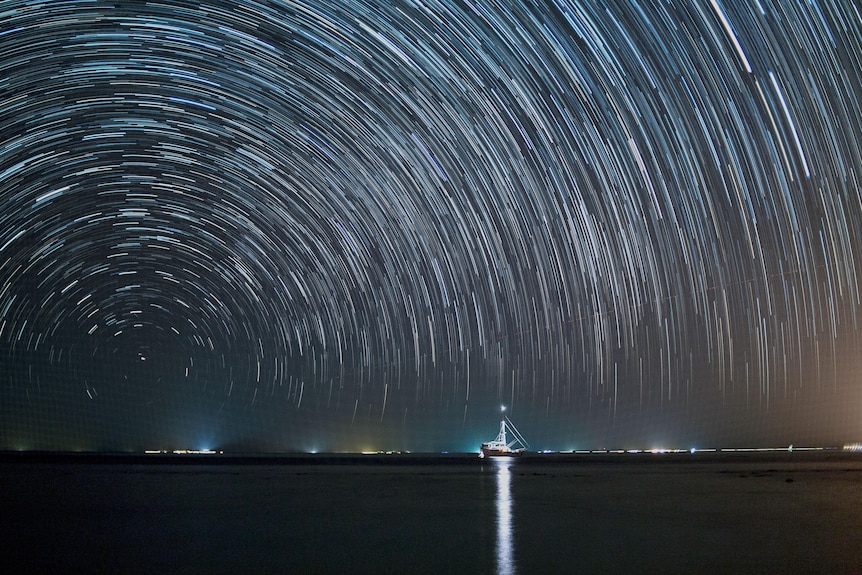 A starry sky above a yacht on the ocean.