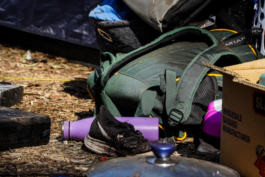 A school backpack, a black shoe, and a purple drink bottle, and a saucepan lid on the ground outside a tent in Bendigo.