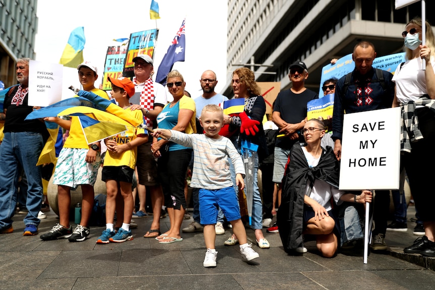 A young child waves a Ukrainian flag in front of protesters holding banners and signs in Sydney.