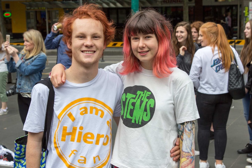 Two young people arm in arm, wearing band t-shirts.