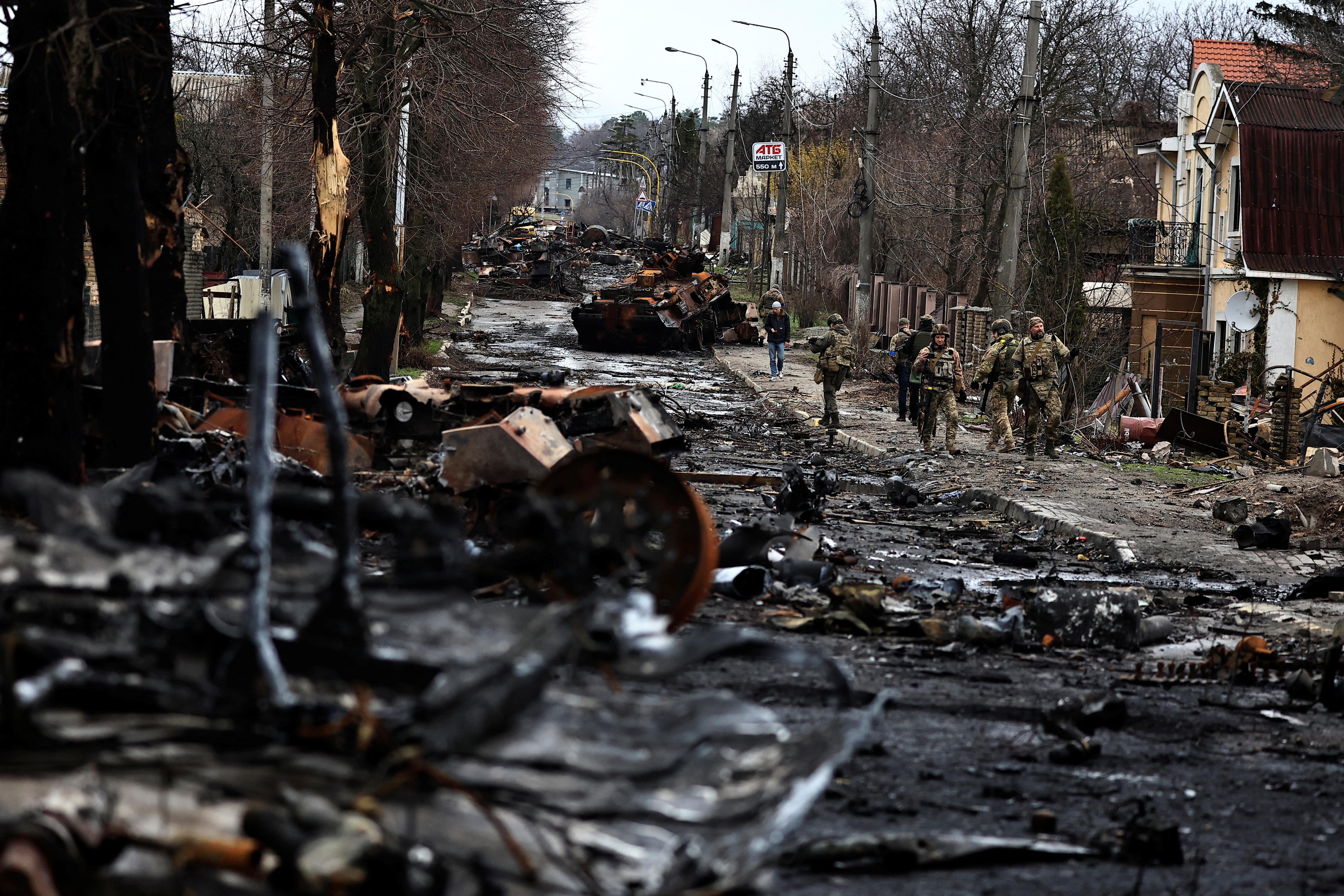 Soldiers walk past a destroyed Russian tank and armoured vehicles on a deserted street.