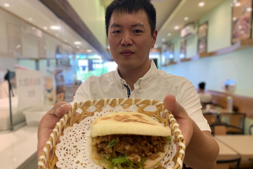 Man in chef jacket holds a pork filled bun up close to the camera in his restaurant