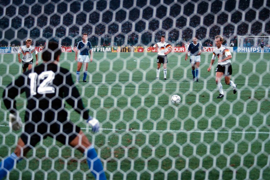 A German footballer runs up to take a penalty in a World Cup final as the goalkeeper stands on the goal line.