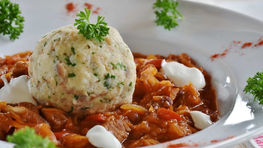 Plate of beef casserole topped with a large herbed dumpling.