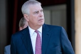 Prince Andrew of the House of Windsor looks sideways, he wears a navy suit and dark tie.