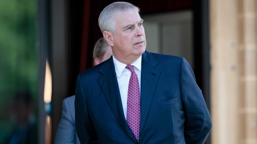 Prince Andrew of the House of Windsor looks sideways, he wears a navy suit and dark tie.