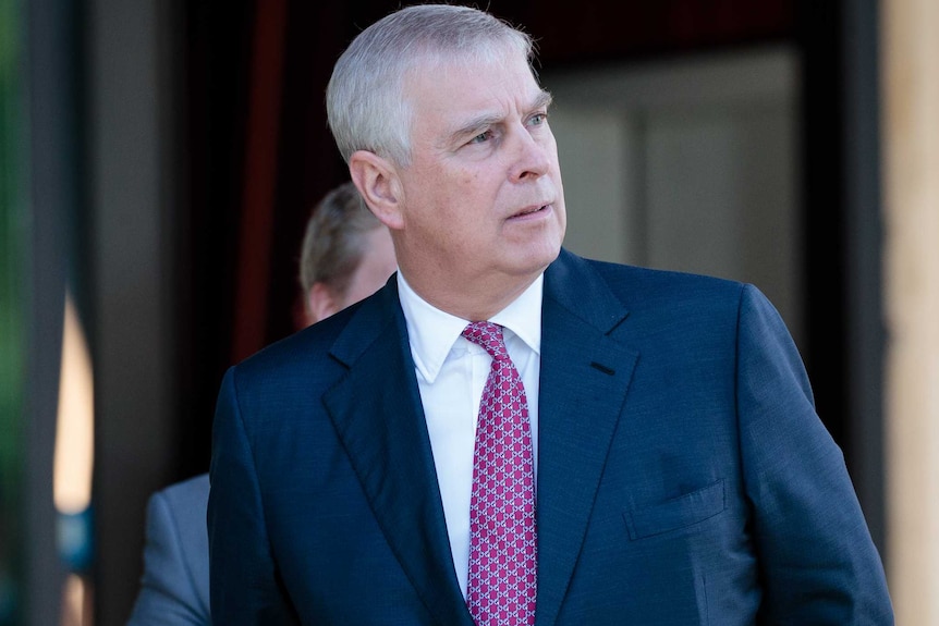 Le prince Andrew de la maison de Windsor a l'air de côté, il porte un costume bleu marine et une cravate foncée.