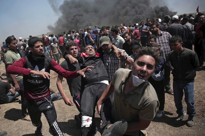 Protesters carry an injured man with smoke in the background.