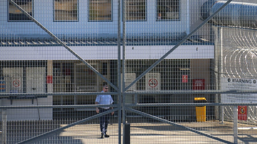 A guard stands behind the entrance to Borallon Training and Correctional Centre in Ironbark