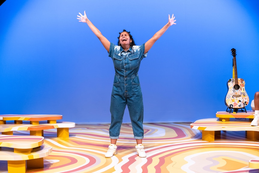 On stage, Zahra Newman, looks upset. She's standing in a denim jumpsuit, arms in the air.